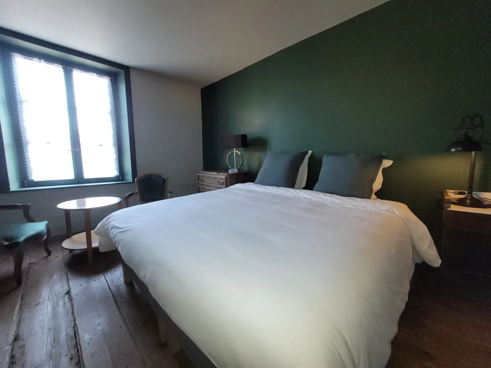 Chambre des Marchands à Maison Cœurdacier, lits préparés, poêle en faïence, fauteuils et lumière naturelle — accès et confort pour les hôtes.