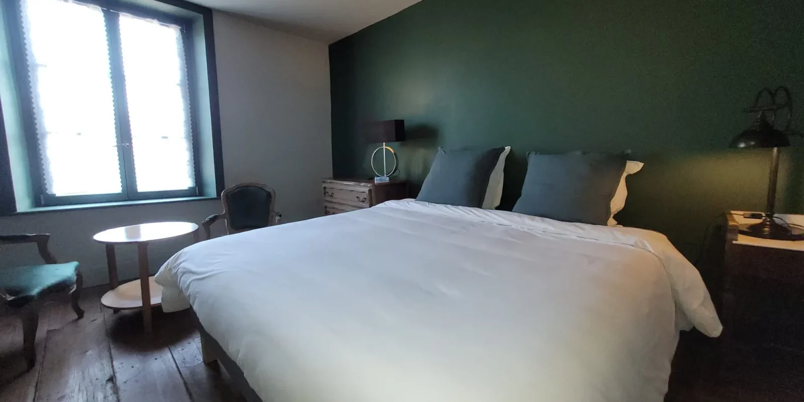 Chambre des Marchands à Maison Cœurdacier, lits préparés, poêle en faïence, fauteuils et lumière naturelle — accès et confort pour les hôtes.