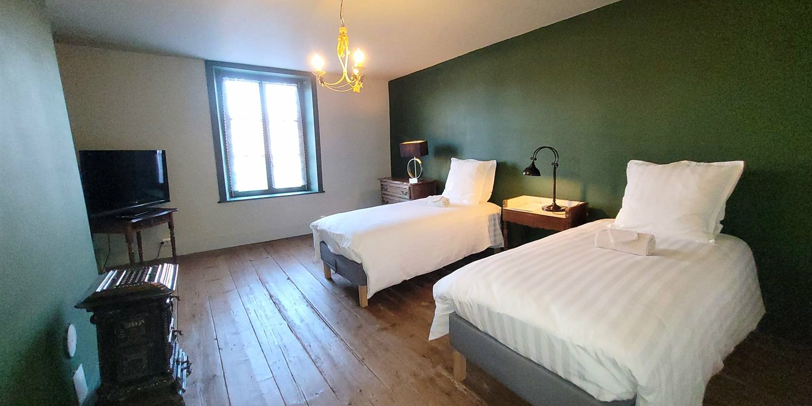 Chambre des Marchands : deux lits simples, murs vert foncé, poêle ancien en fonte et parquet