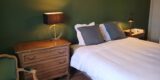 Chambre aux murs vert foncé : lit aux oreillers gris, commode ancienne et lampe de chevet